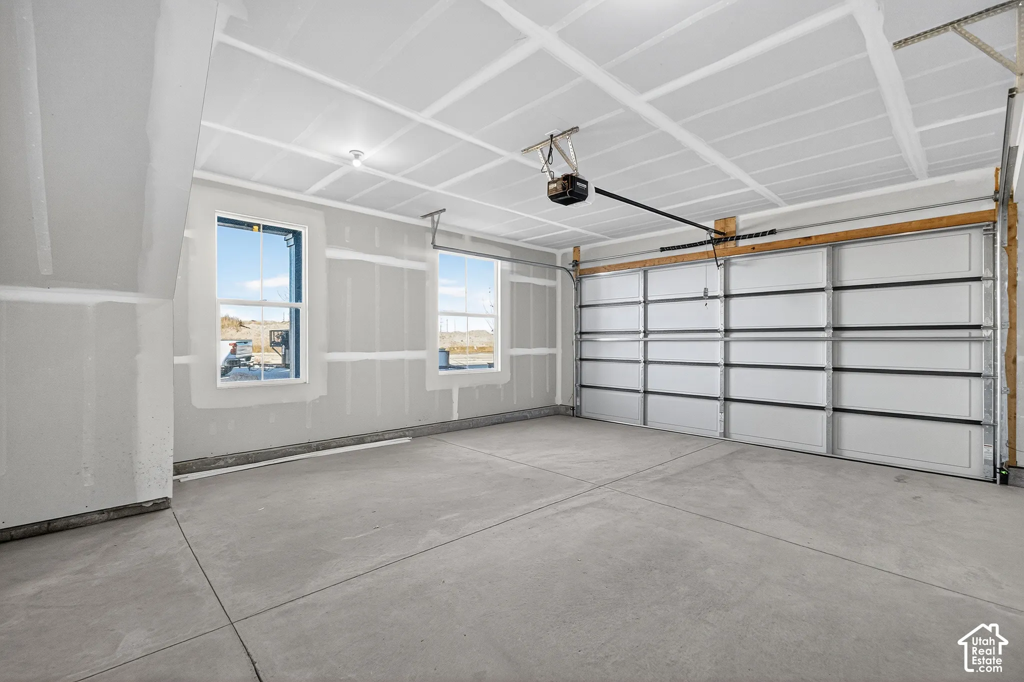 Finished garage space featuring smooth drywall walls, two double-pane windows, a concrete floor, and an automated overhead door
