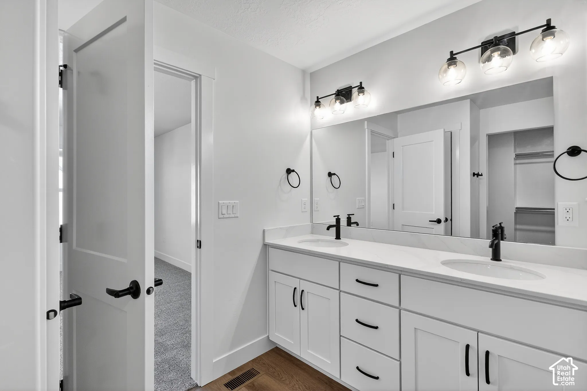 Double vanity featuring white cabinetry, light-toned countertop, dual under-mount sinks, matte black hardware, and two multi-light fixtures