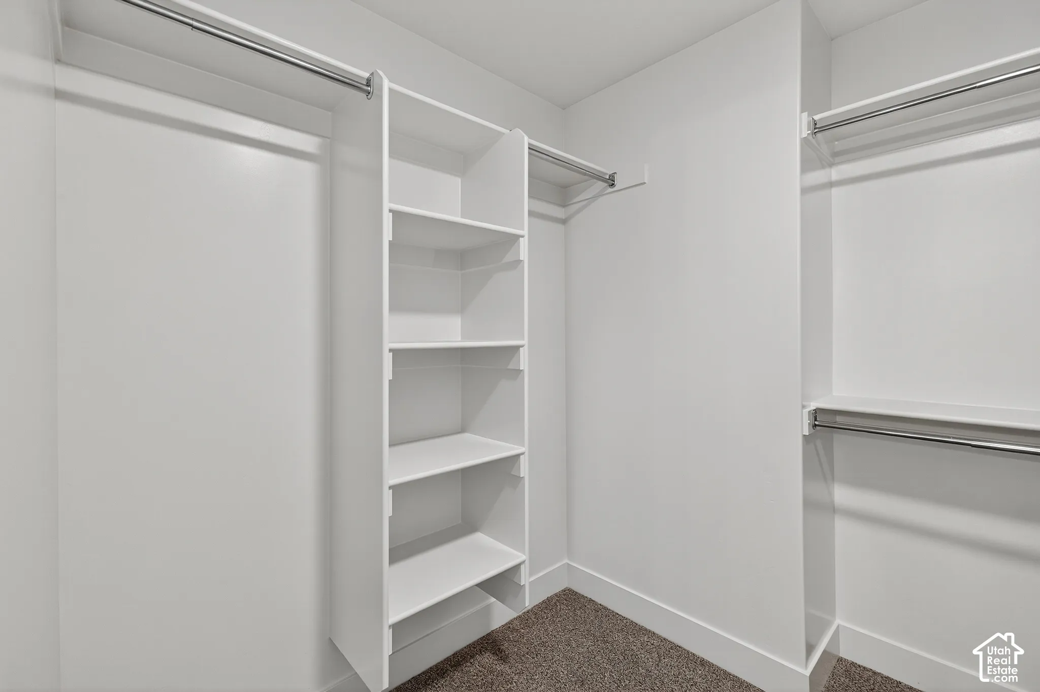 Walk-in closet featuring white built-in shelving, dual-tier metal hanging rods, and neutral-tone carpeting