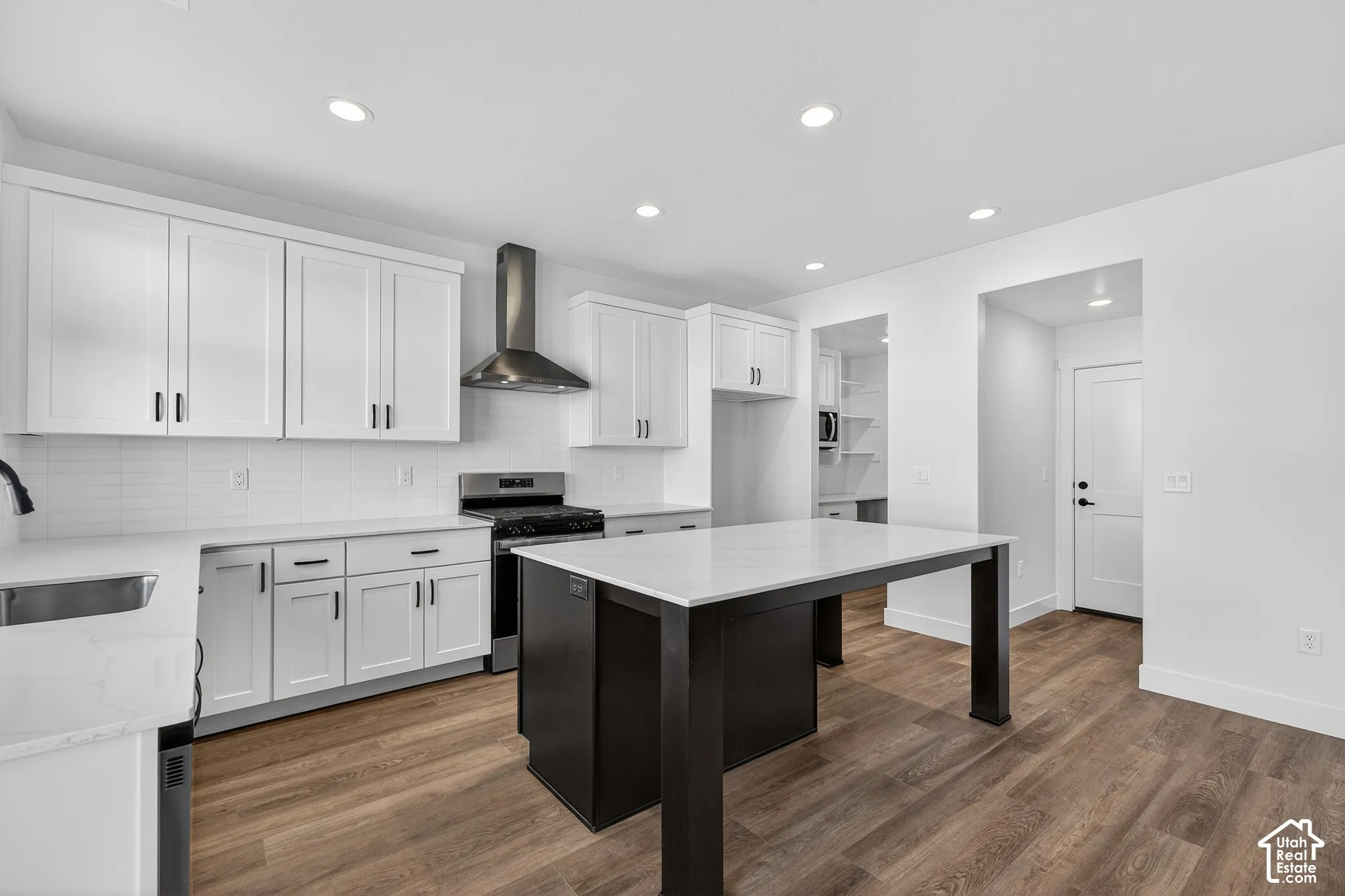 Kitchen featuring white cabinetry, solid-surface countertops, center island with a dark finish, stainless steel range hood, and wood-finish flooring