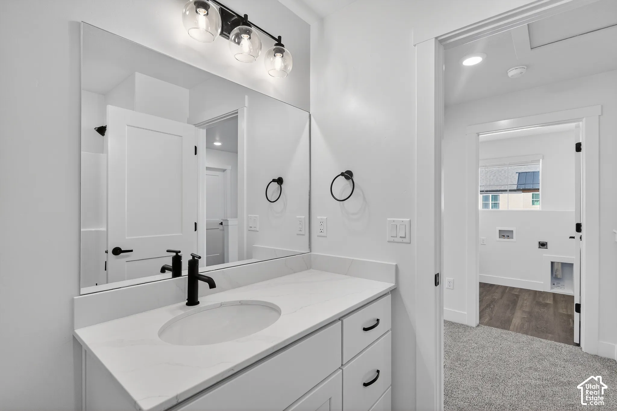 Vanity with a solid surface countertop, undermount sink, matte black faucet, and three-light glass globe fixture, complemented by a large wall-mounted mirror