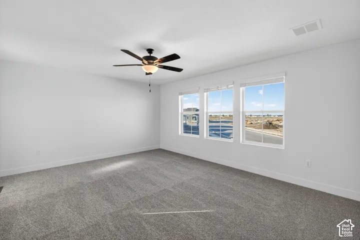 Room featuring neutral wall-to-wall carpeting, three grid-pattern windows, and a multi-blade ceiling fan with integrated light fixture