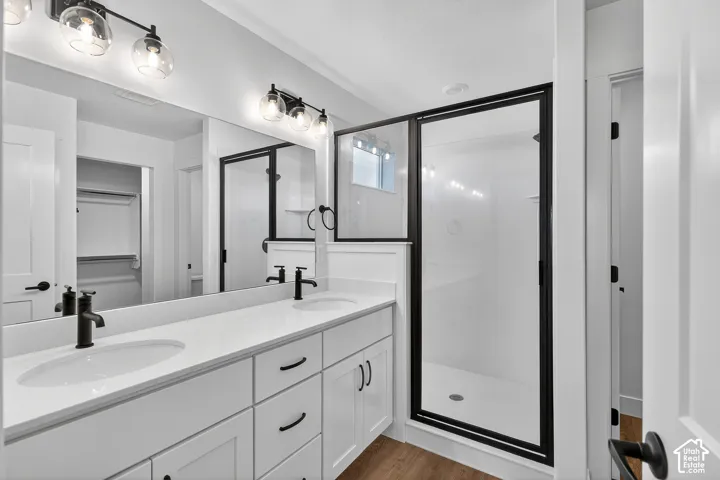 Dual-sink vanity with white cabinetry, light-toned countertop, and matte black hardware, paired with a glass-enclosed shower featuring a matte black frame and wood-finish flooring