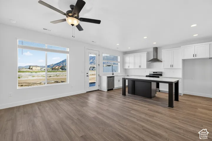 Open-concept kitchen featuring white cabinetry, a contrasting dark kitchen island, stainless steel range hood, recessed lighting, and wood-finish flooring