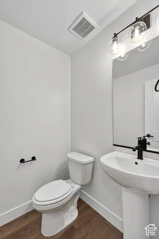 Pedestal sink with matte black faucet, wall-mounted mirror, three-light globe vanity fixture, and wood-finish flooring
