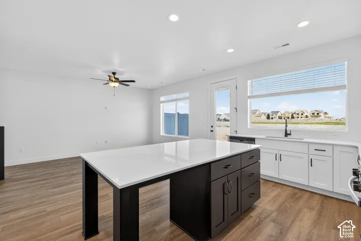 Kitchen featuring an expansive island with a stone-finish countertop, white cabinetry with matte black hardware, recessed ceiling lighting, wood-finish flooring, and a ceiling fan