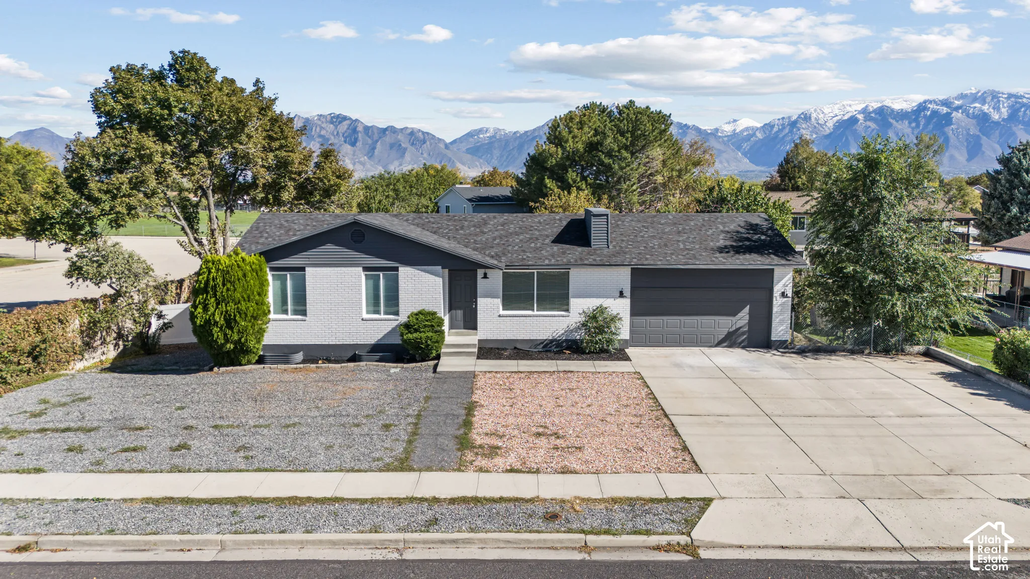 Single-level residence with a painted brick exterior, attached two-car garage, concrete driveway, and prominent mountain backdrop