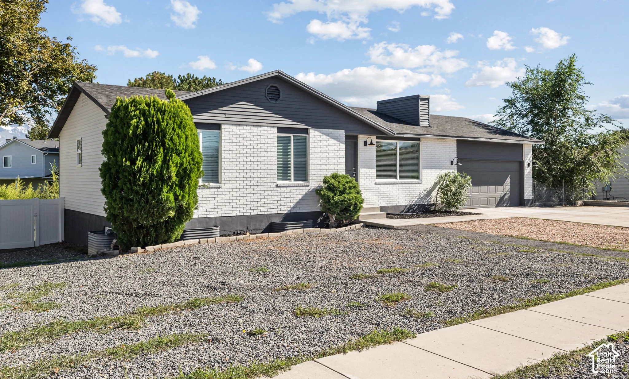 Single-level exterior featuring white-painted brick and horizontal siding, a gabled roofline, an attached garage, and a concrete driveway