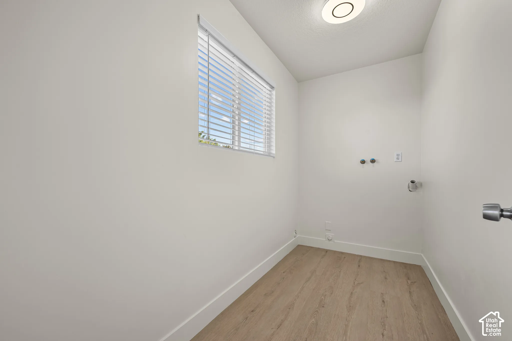 Utility area featuring wood-finish flooring, a horizontal window with adjustable blinds, and integrated plumbing hookups