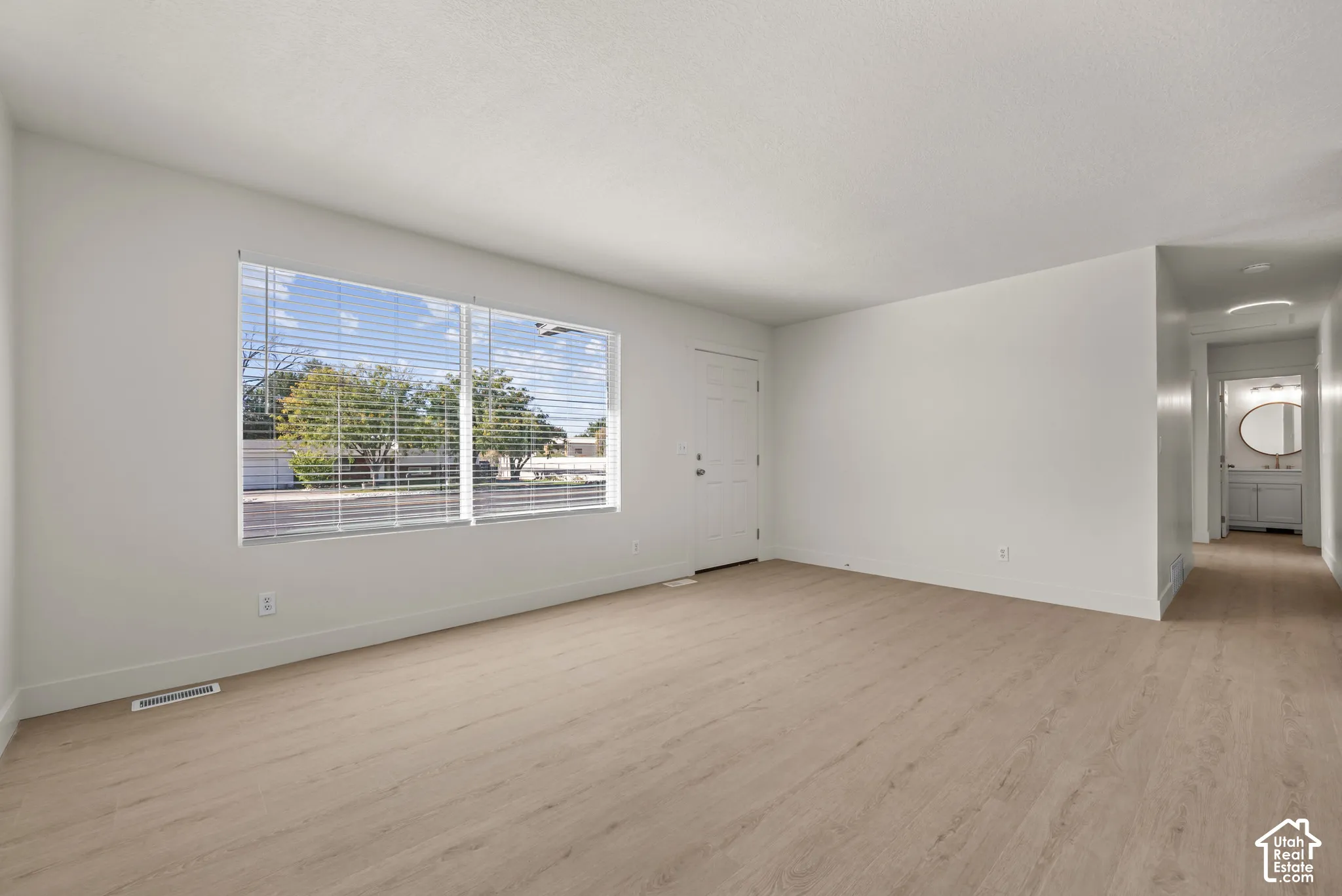 Neutral-toned wall paint, wood-finish flooring, and large window with horizontal blinds