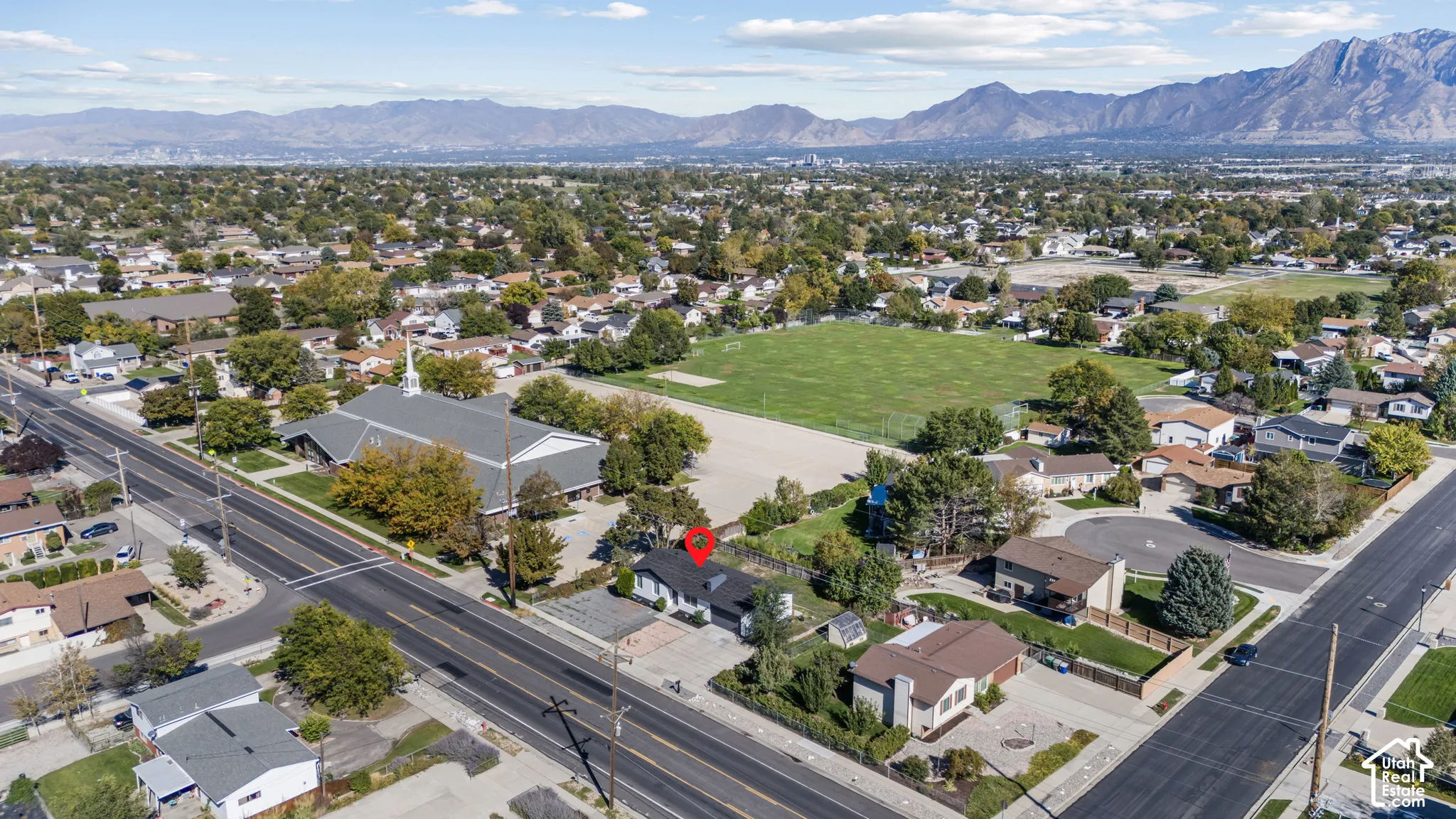 Aerial perspective of a detached single-family residence featuring a dark-toned asphalt shingle roof, mature landscaping, and an expansive mountain range backdrop