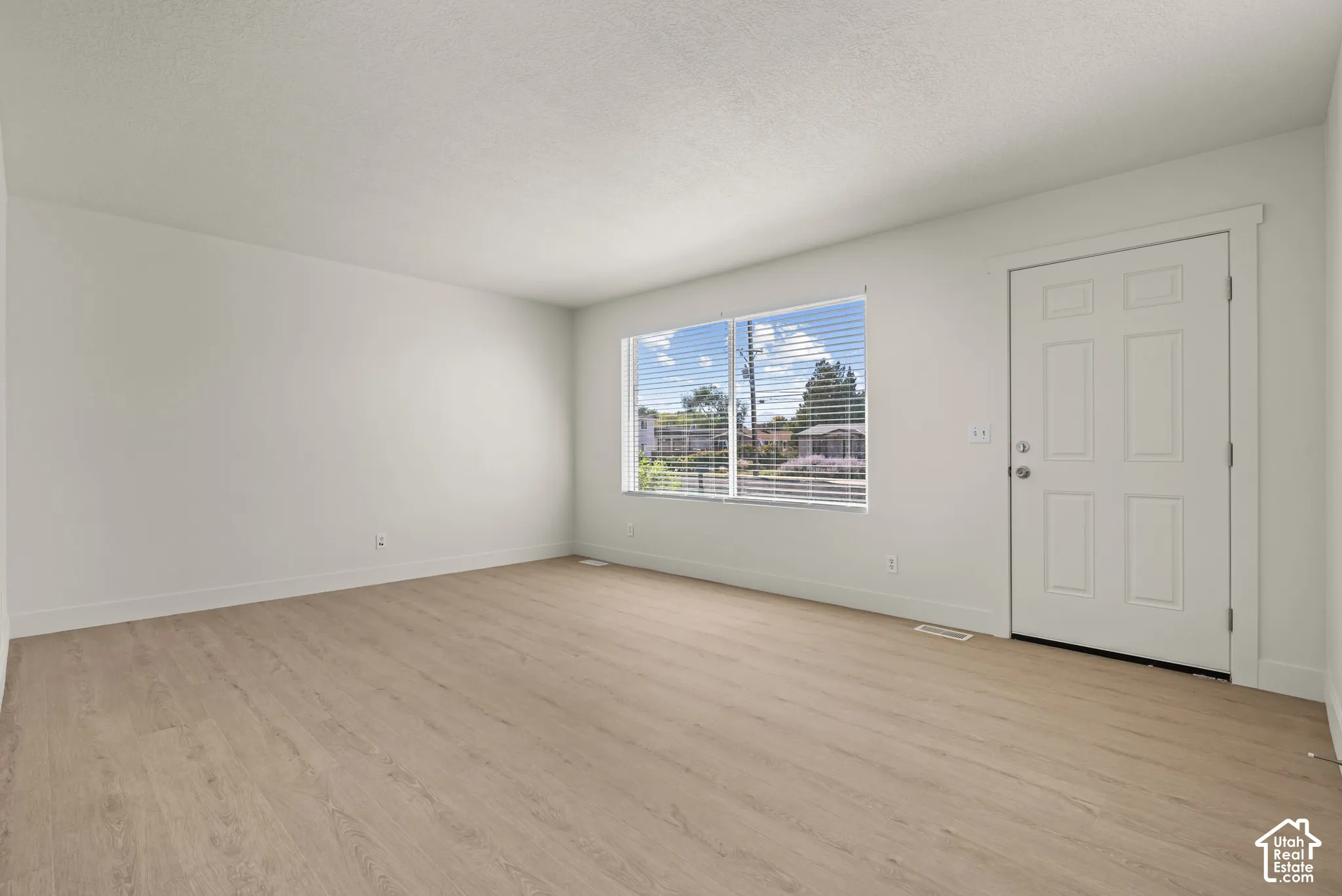 Interior space featuring wood-finish flooring, a six-panel exterior door, and a large window with horizontal blinds