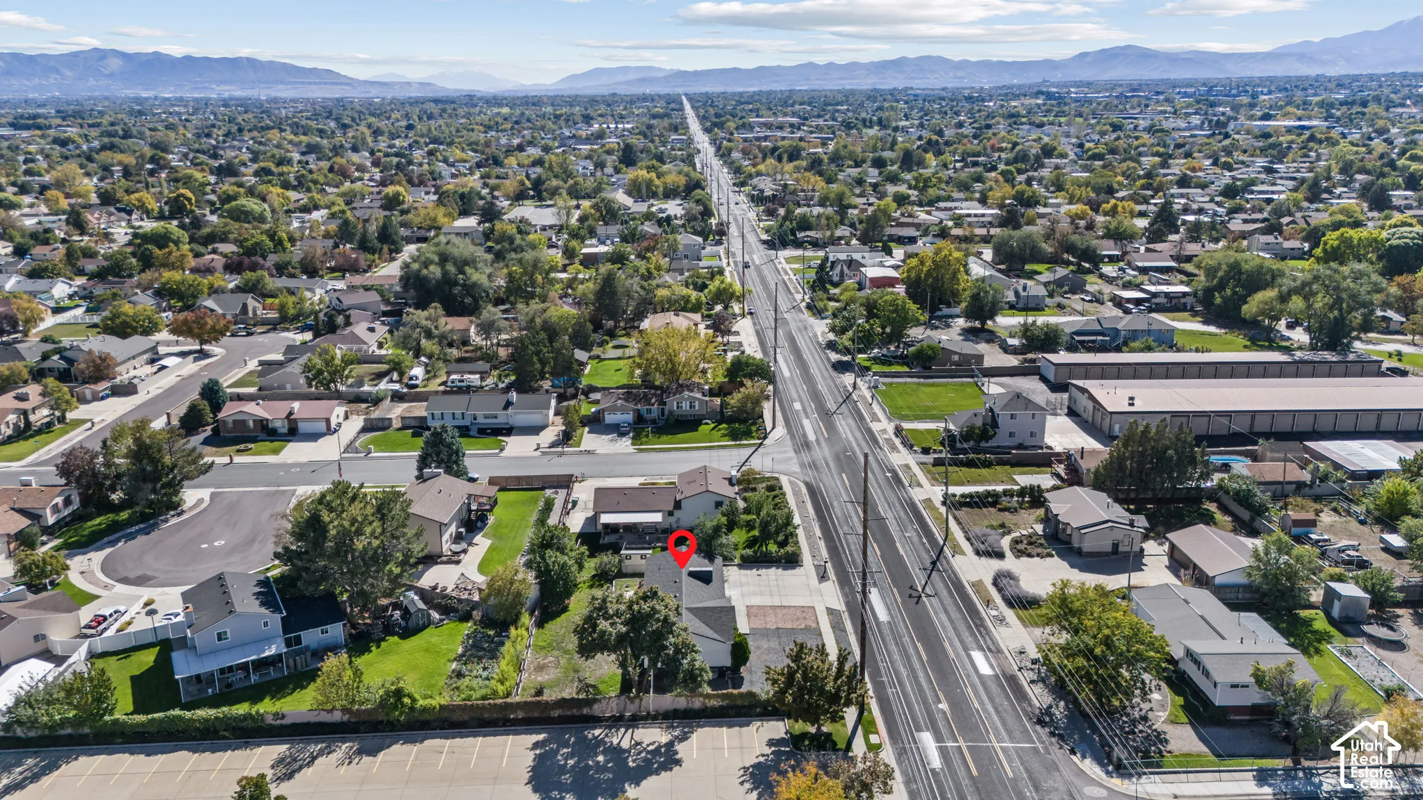 Aerial perspective featuring a detached residential property situated on a corner lot with mature landscaping, a paved driveway, and mountain scenery in the background