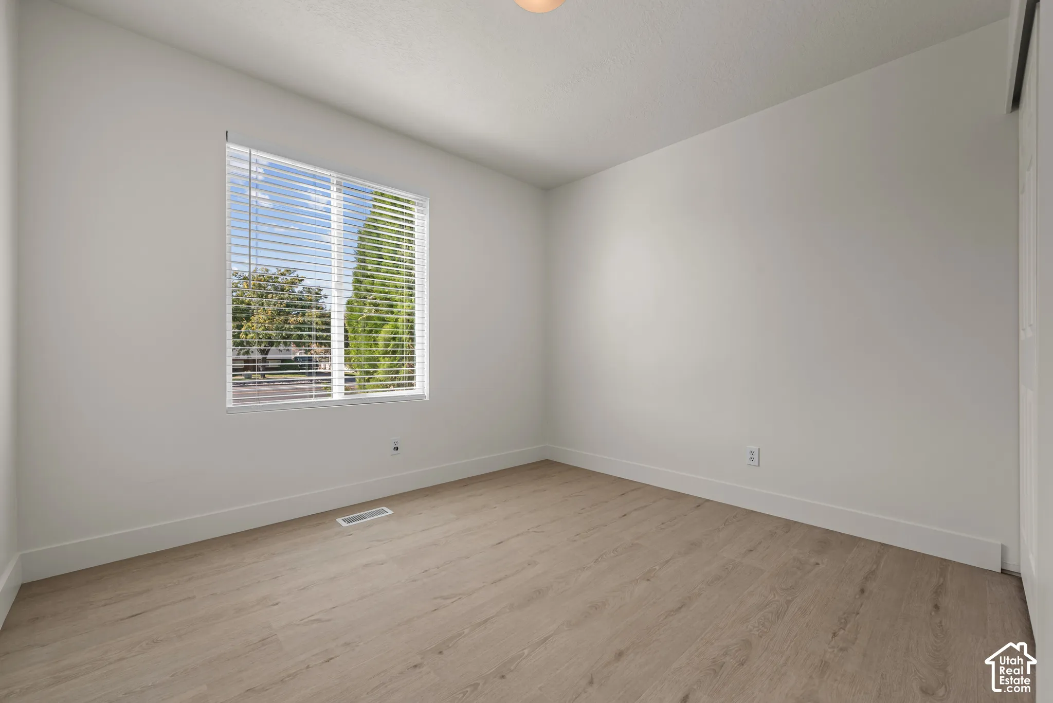 Neutral interior room featuring wood-finish flooring, white walls, and a window with horizontal blinds