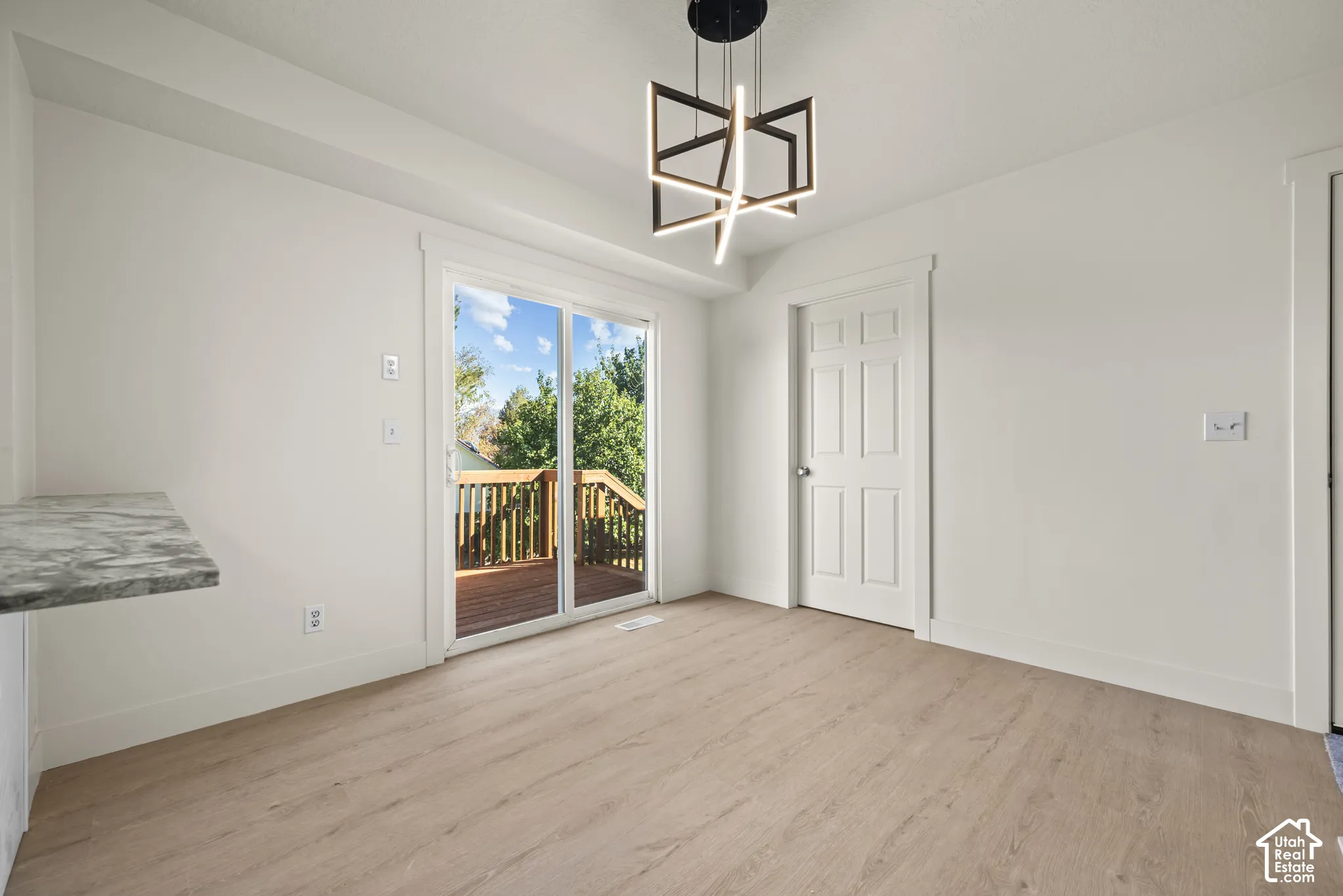 Light-toned wood-finish flooring, geometric architectural pendant lighting, sliding glass door, and a built-in stone-patterned counter