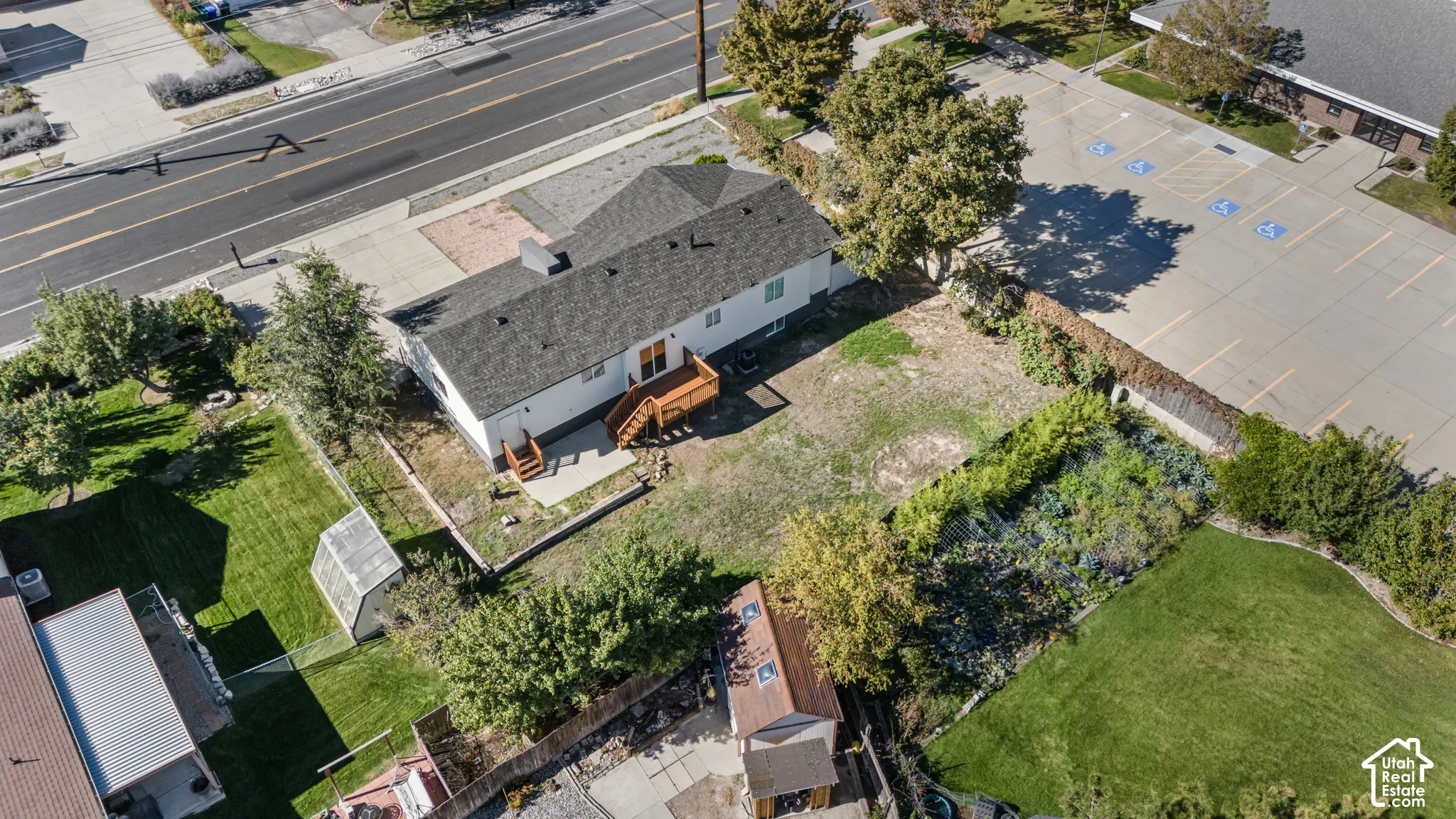 Aerial perspective of property featuring a detached wood-frame structure, raised wooden deck, rear patio, and expansive lawn area with mature trees