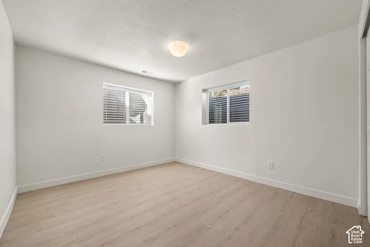 Neutral-toned room featuring wood-finish flooring, white walls, dual windows, and a central dome-style ceiling light fixture