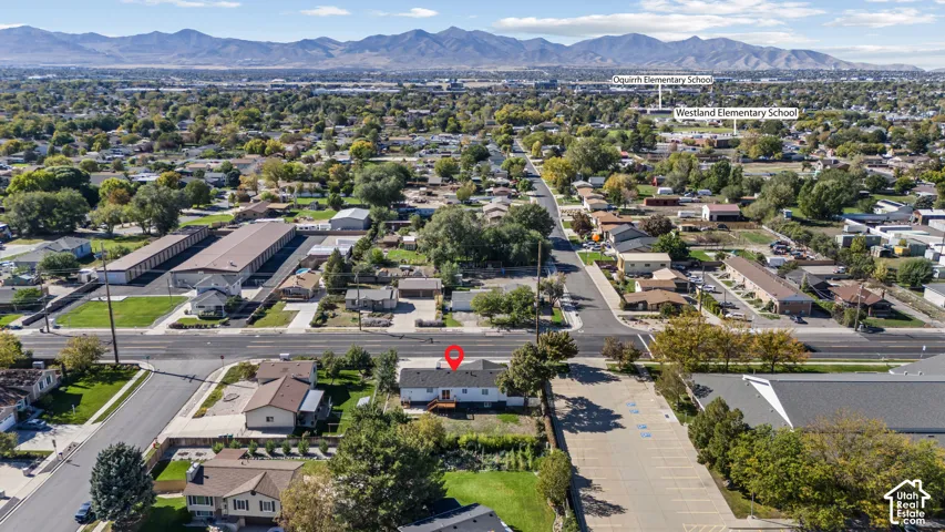 Aerial perspective featuring a single-story residence with a wood deck, set against a backdrop of mountain ranges and established local landscaping