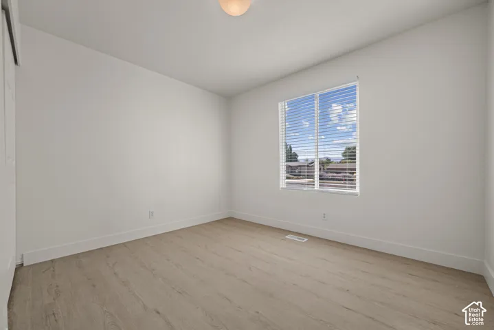 Interior room featuring light-toned wood-finish flooring, white wall paint, a single window with horizontal blinds, and a built-in closet with sliding doors
