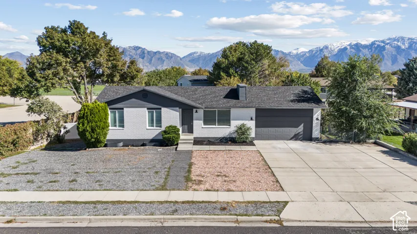 Single-level residence with a painted brick exterior, attached two-car garage, concrete driveway, and prominent mountain backdrop