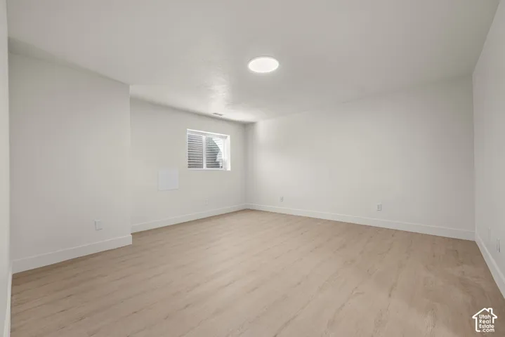 Neutral-toned interior space featuring wood-finish flooring, white walls, flush-mount ceiling lighting, and a recessed window with a light well