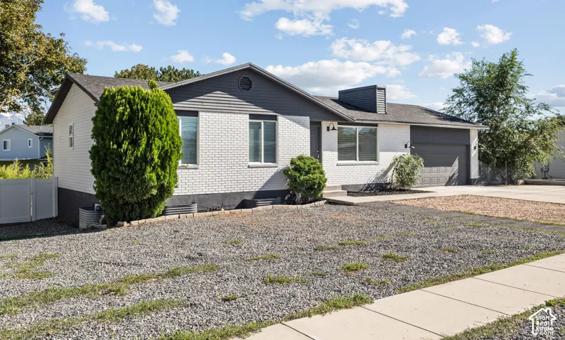 Single-level exterior featuring white-painted brick and horizontal siding, a gabled roofline, an attached garage, and a concrete driveway