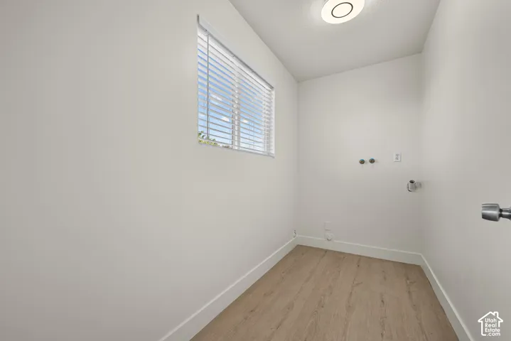 Utility area featuring wood-finish flooring, a horizontal window with adjustable blinds, and integrated plumbing hookups