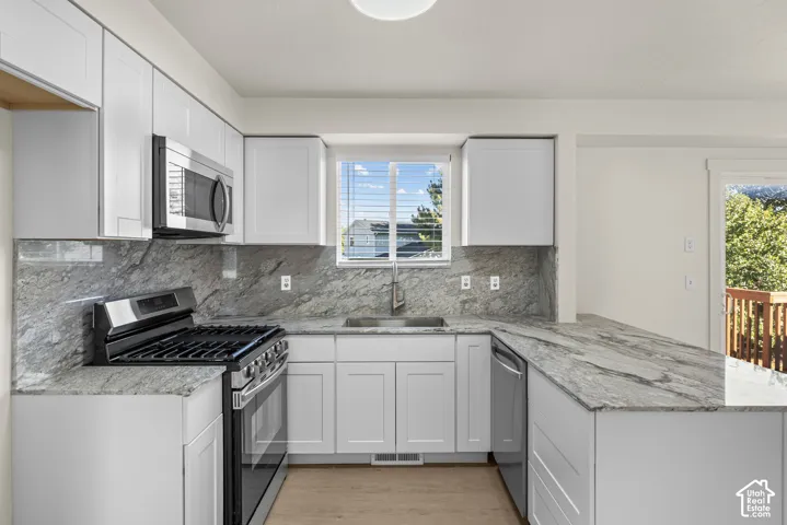 Kitchen featuring white cabinetry, stone countertops with matching full-height backsplash, stainless steel appliances, and wood-finish flooring