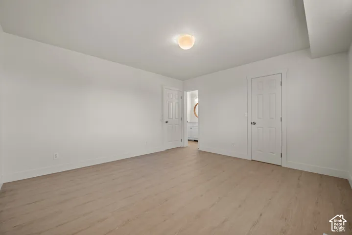 Neutral-toned room featuring wood-finish flooring, crisp white wall paint, two six-panel interior doors, and a flush-mount ceiling fixture