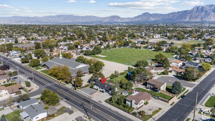 Aerial perspective of a detached single-family residence featuring a dark-toned asphalt shingle roof, mature landscaping, and an expansive mountain range backdrop