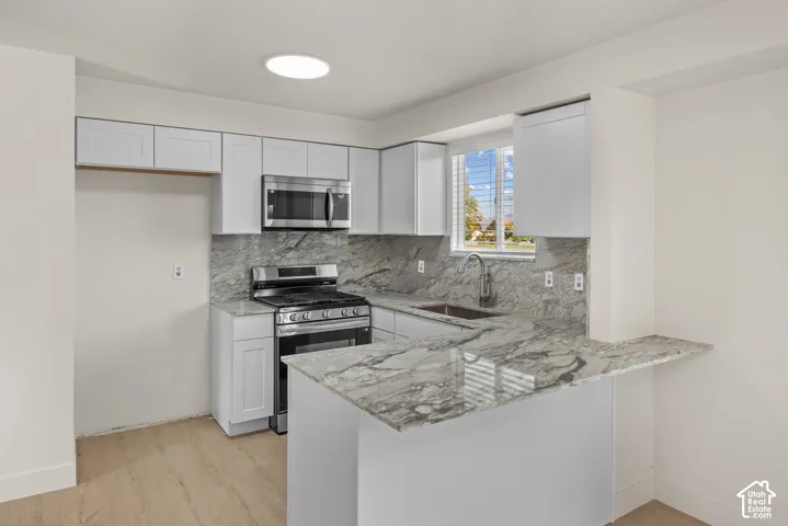 Kitchen featuring white shaker-style cabinetry, stone countertops, stone tile backsplash, stainless steel appliances, and wood-finish flooring
