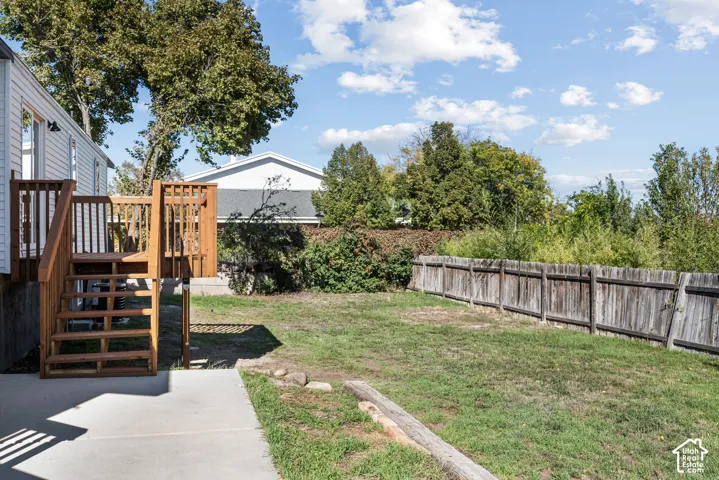 Backyard featuring a wood-tone raised deck with staircase, concrete patio, grass lawn, and wood privacy fencing