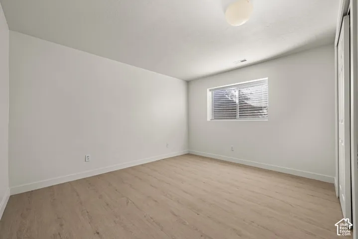 Neutral-toned room featuring wood-finish flooring, a single window, a ceiling-mounted light fixture, and a sliding-panel closet door