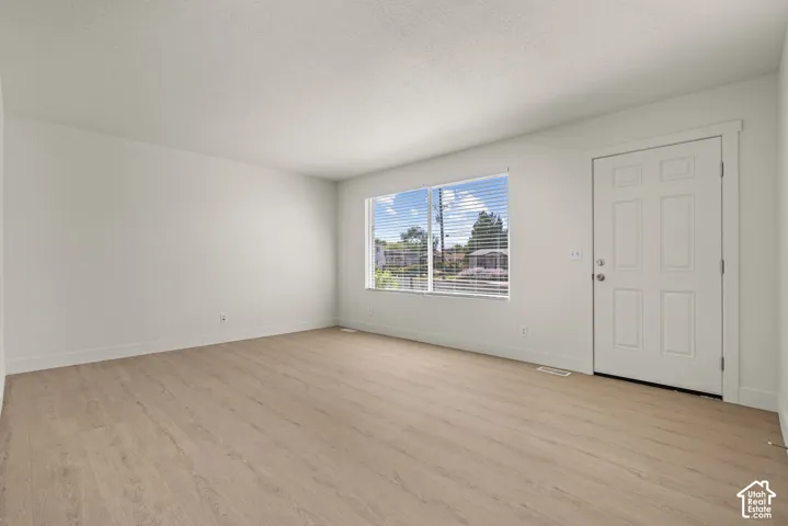 Interior space featuring wood-finish flooring, a six-panel exterior door, and a large window with horizontal blinds