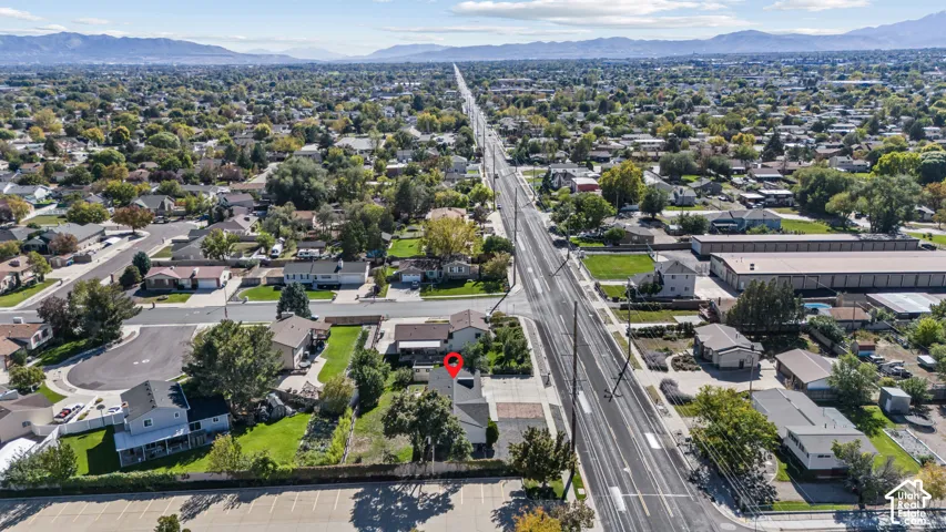 Aerial perspective featuring a detached residential property situated on a corner lot with mature landscaping, a paved driveway, and mountain scenery in the background