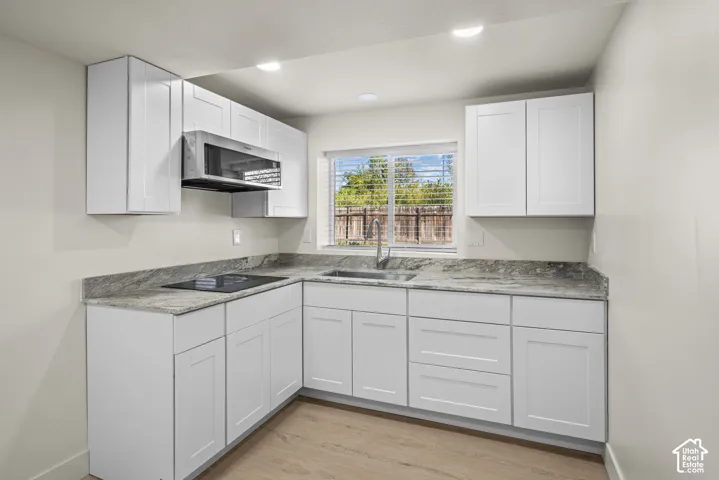 Kitchen featuring white shaker-style cabinetry, stone-surface countertops, a stainless steel sink with a pull-down faucet, an integrated cooktop, and wood-finish flooring