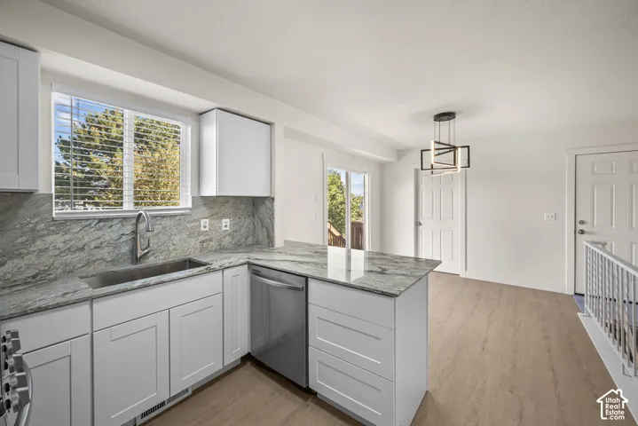 Kitchen featuring white cabinetry, stone countertops with matching backsplash, stainless steel under-mount sink, integrated stainless steel dishwasher, and geometric pendant lighting