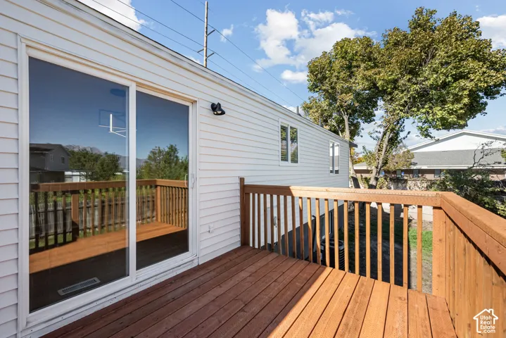 Elevated wood deck featuring stained railing and sliding glass door entry with exterior wall-mounted lighting