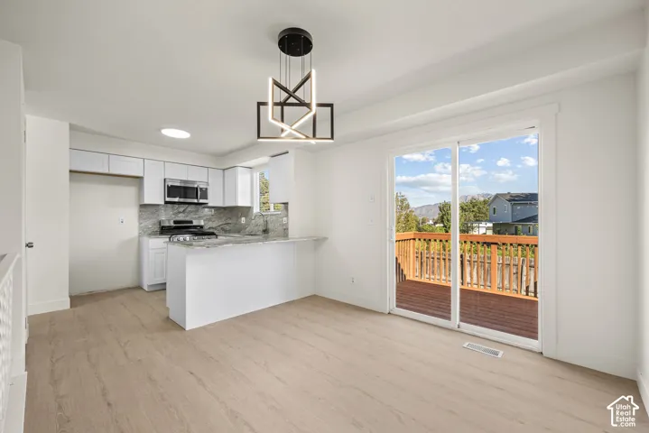 Kitchen featuring white cabinetry, stone-surface countertops, built-in stainless steel microwave, geometric pendant lighting, and sliding glass doors with wood-deck access