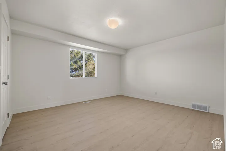 Neutral-toned room featuring wood-finish flooring, a single-pane window with installed blinds, and a centered flush-mount ceiling light fixture