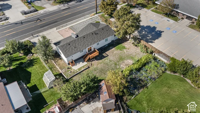Aerial perspective of property featuring a detached wood-frame structure, raised wooden deck, rear patio, and expansive lawn area with mature trees