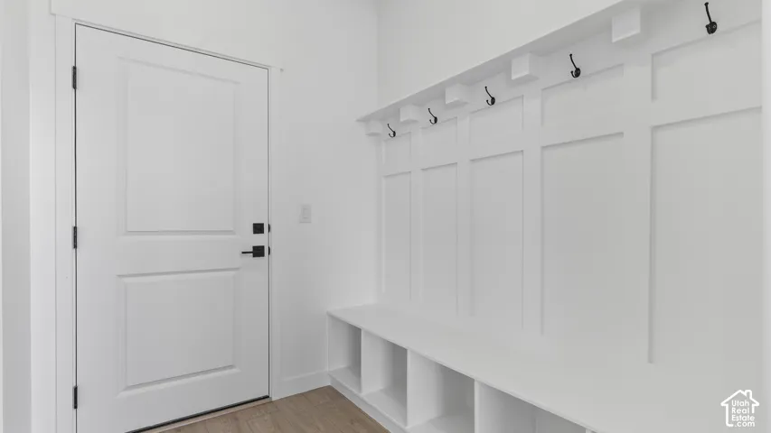 Built-in storage bench featuring crisp white millwork, decorative wall paneling, integrated coat hooks, and wood-finish flooring