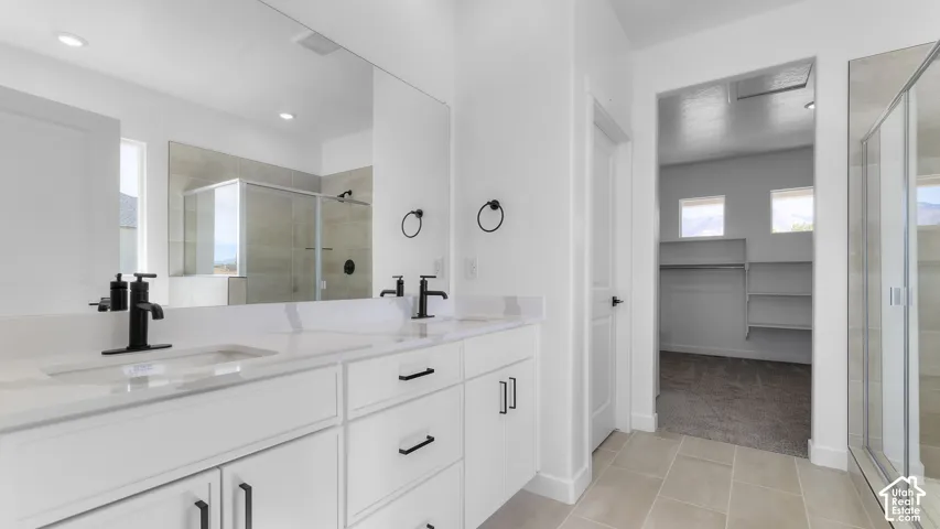 Dual-sink vanity with white cabinetry, quartz countertop, matte black fixtures, and large frameless mirror, featuring a walk-in shower with tiled surround and ceramic tile flooring