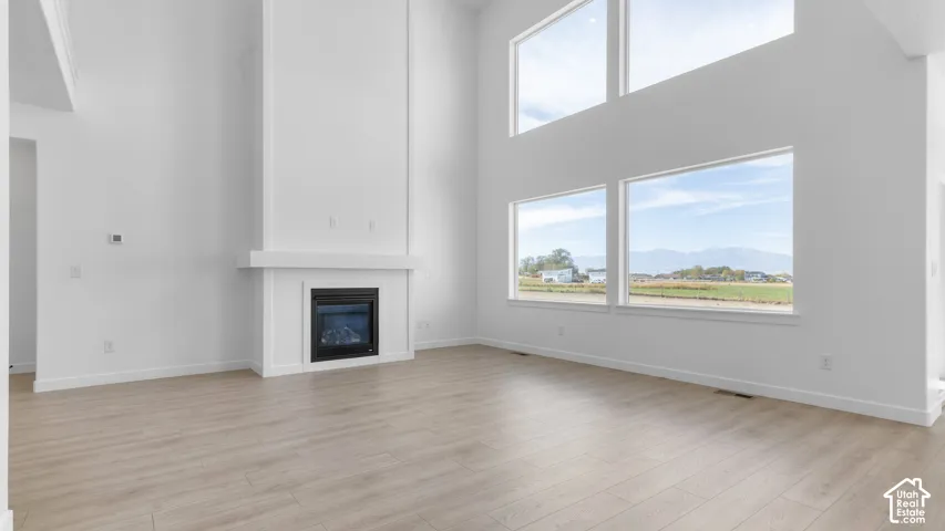 Two-story ceiling, floor-to-ceiling fireplace with mantel, oversized windows, wood-finish flooring, and mountain backdrop