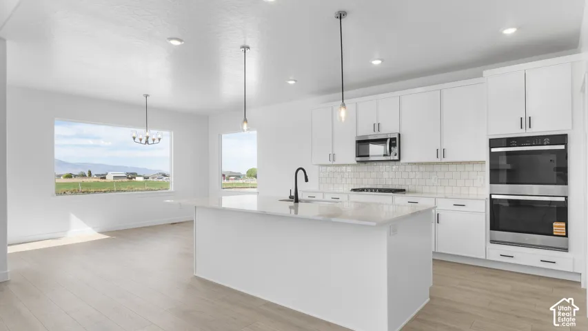 Kitchen featuring white cabinetry, quartz countertops, a central island with a matte black faucet, stainless steel double wall ovens, and wood-finish flooring