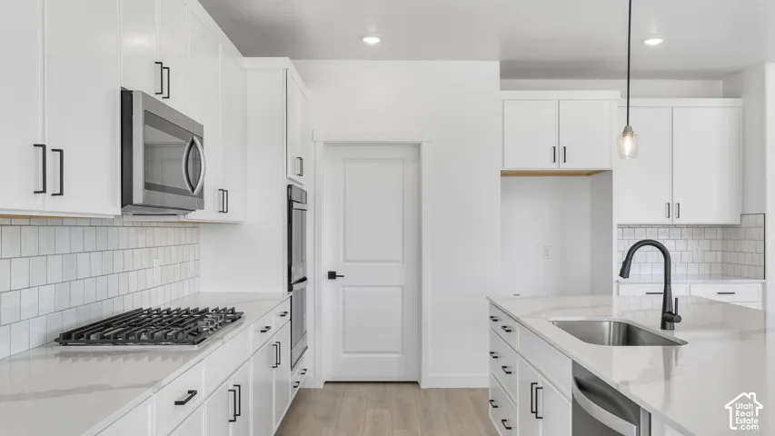 Kitchen featuring white cabinetry with matte black hardware, stone-surface countertops, subway tile backsplash, stainless steel built-in appliances, and a central island with a pull-down faucet