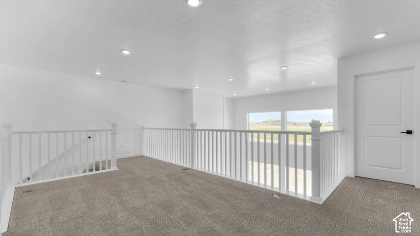 Interior space featuring carpeted flooring, white baluster railings, recessed lighting, and a single-panel interior door with matte black hardware