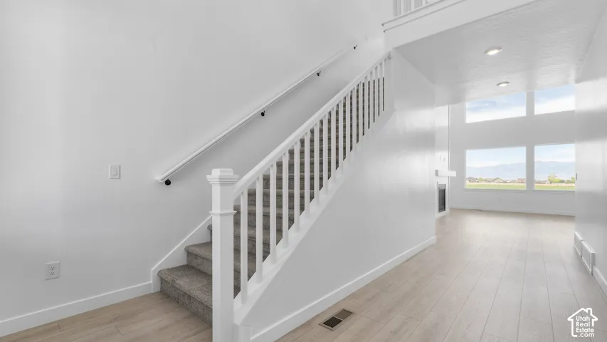 Staircase with white railing and carpeted treads, wood-finish flooring, two-story windows, and mountain backdrop