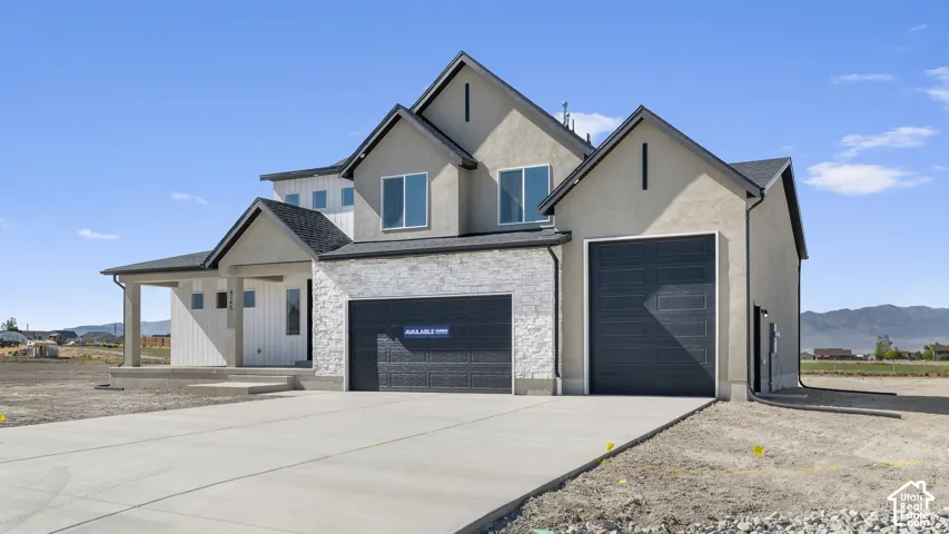 Multi-gabled exterior featuring stucco siding, vertical board-and-batten accents, stone veneer detailing, two dark-finish garage doors, and a covered front porch