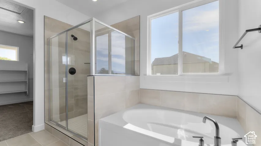 Walk-in shower with matte black fixtures, neutral tile surround, soaking tub with deck-mounted faucet, and window providing natural light
